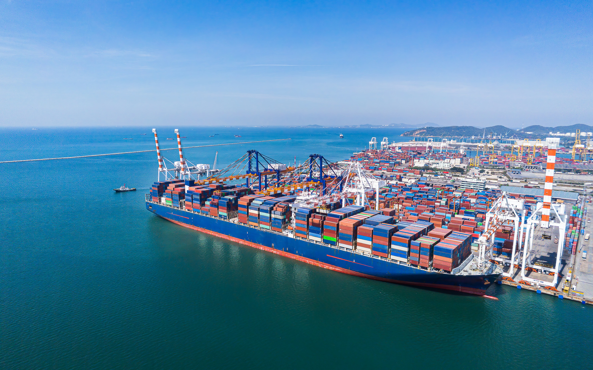 Vue d’un grand porte-conteneurs au port, chargement de conteneurs colorés prêt pour un déménagement outre-mer. Déménagement outre-mer guide pratique.